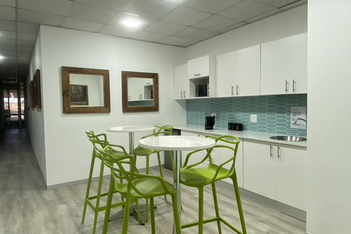 A modern office kitchenette featuring white cabinetry, a blue tiled backsplash, integrated sink, and recessed ceiling lighting.