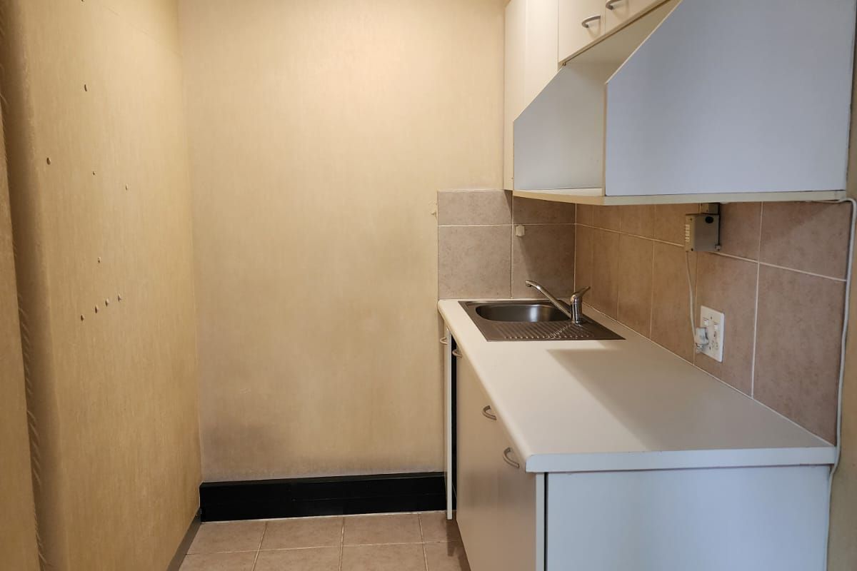 A compact office kitchenette featuring white cabinetry, a stainless steel sink, tiled backsplash, and tiled flooring.