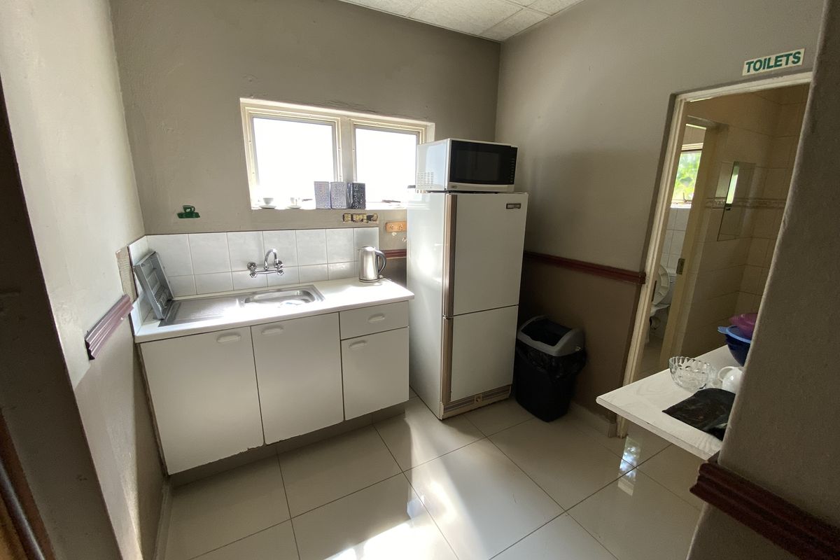 A functional kitchenette area featuring built-in cabinetry, a stainless steel sink, and tiled flooring, with direct access to an adjacent restroom facility.
