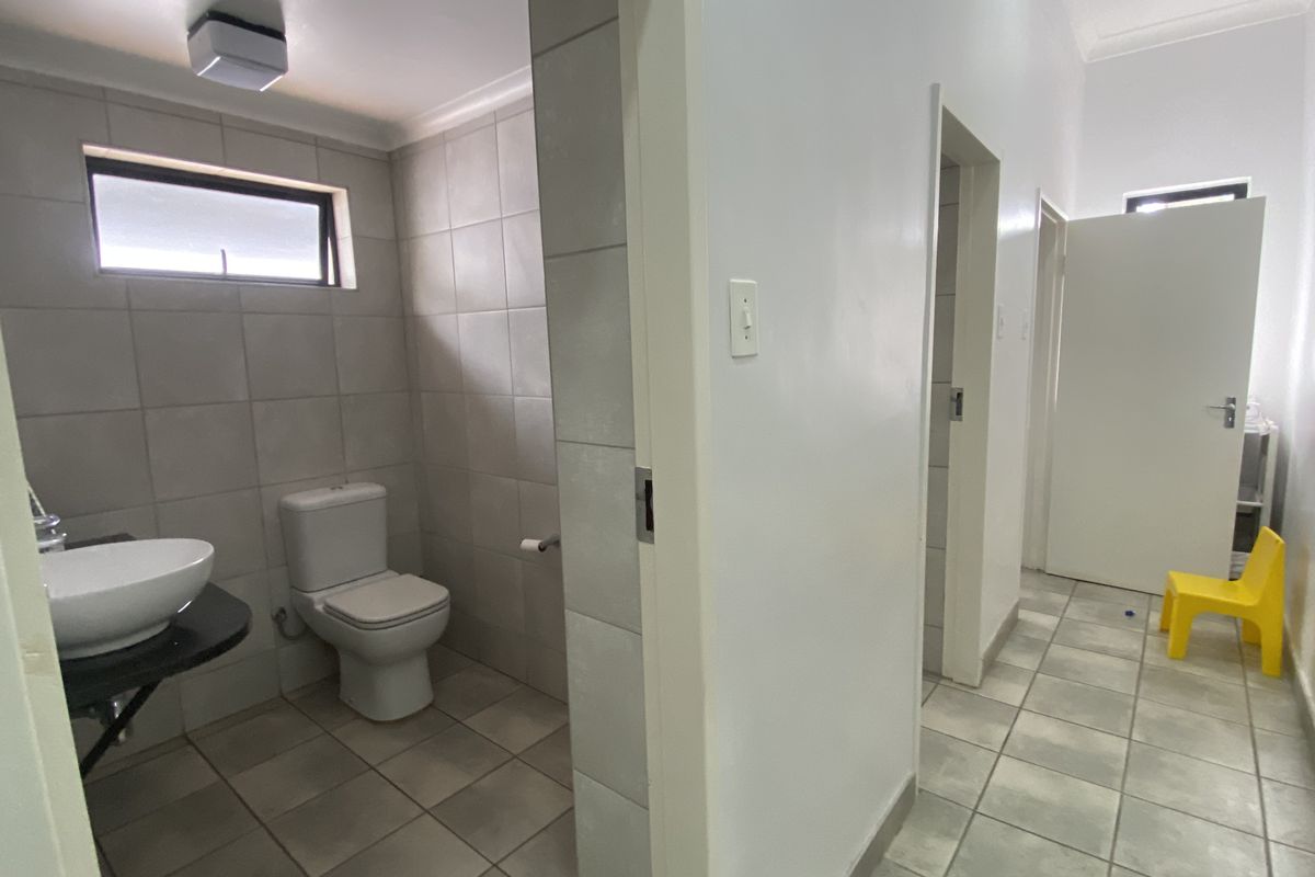 A functional commercial bathroom featuring tiled walls and flooring, a modern vessel sink, and a private toilet cubicle.