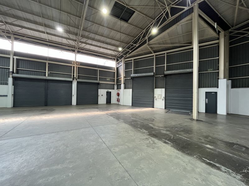 Spacious industrial warehouse unit featuring high ceilings, concrete flooring, multiple roller shutter doors, and integrated fire safety equipment.