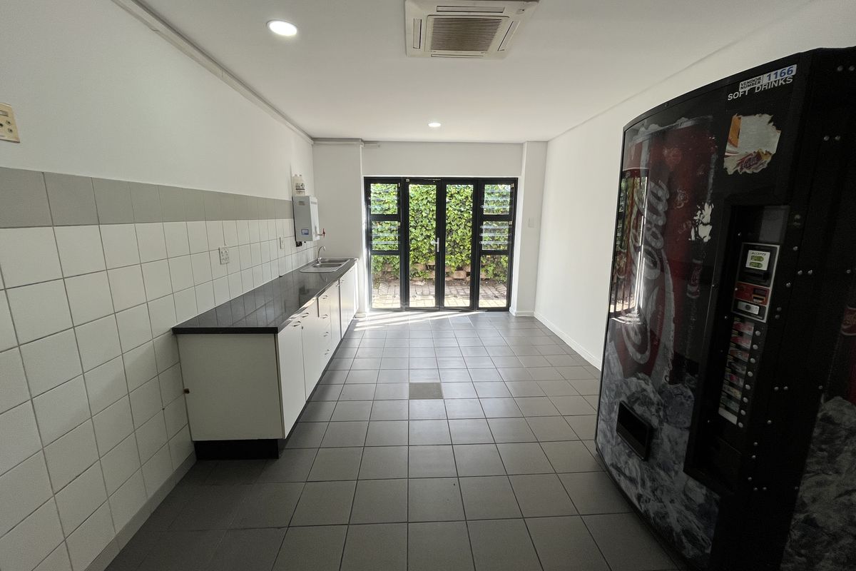 A clean, functional kitchenette area featuring built-in cabinetry, a sink, tiled flooring, and direct access to an outdoor garden space through glass doors.