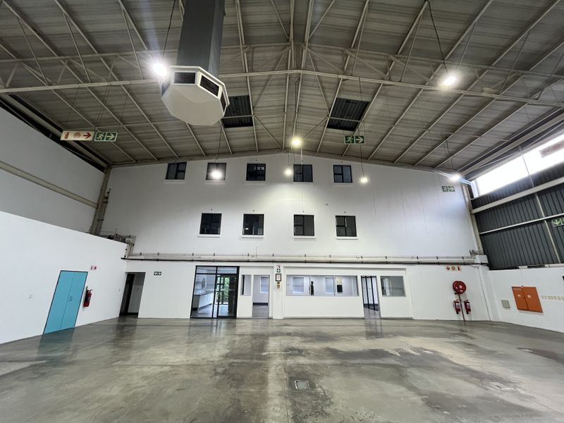 Spacious industrial warehouse area featuring high ceilings with exposed steel trusses, polished concrete flooring, integrated office partitioning, and essential fire safety equipment.