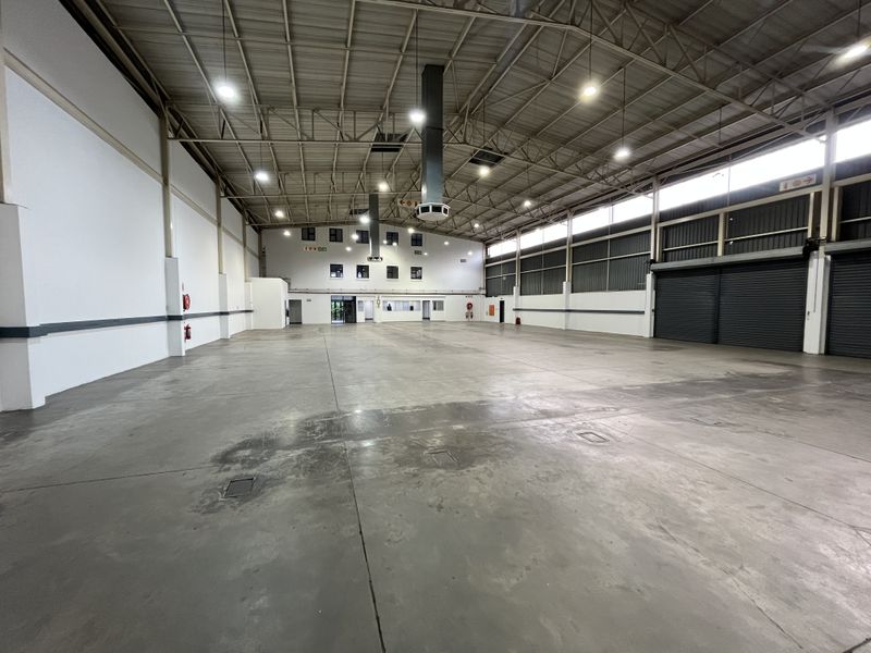 Spacious industrial warehouse featuring high ceilings, concrete flooring, roller shutter doors, and integrated ventilation and lighting systems.