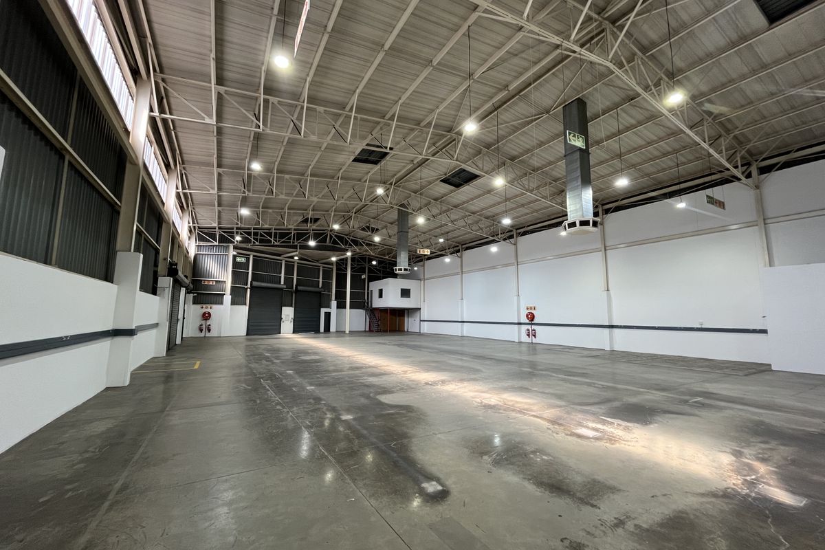 Spacious industrial warehouse featuring high ceilings with exposed steel trusses, polished concrete flooring, roller shutter access, and integrated mezzanine office space.