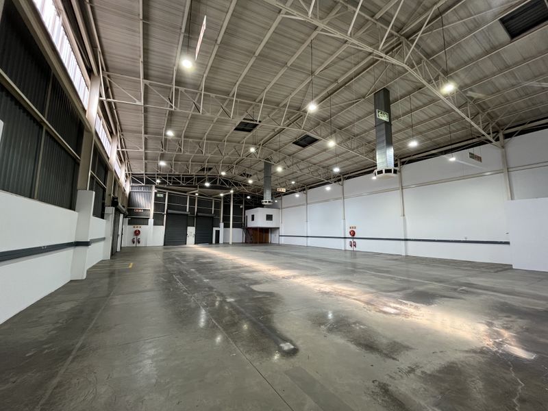 Spacious industrial warehouse featuring high ceilings with exposed steel trusses, polished concrete flooring, roller shutter access, and integrated mezzanine office space.