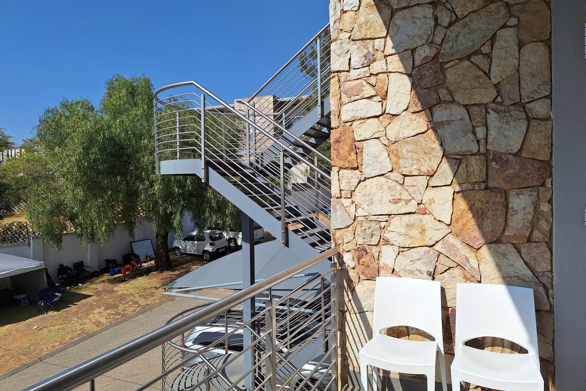 Exterior view of a modern office building featuring a stone-clad facade and a stainless steel external staircase leading to an upper level balcony.