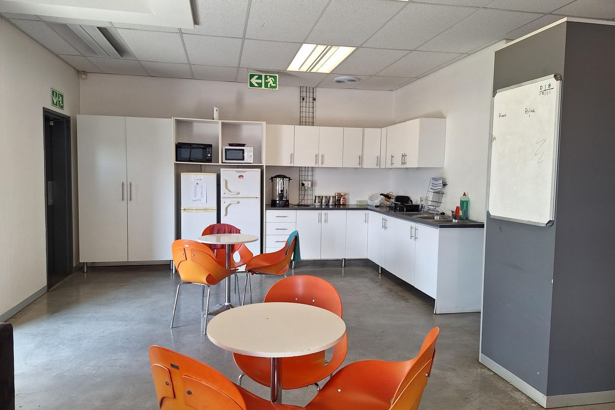 A functional office kitchenette featuring white cabinetry, laminate countertops, a stainless steel sink, and a suspended acoustic tile ceiling with integrated lighting.