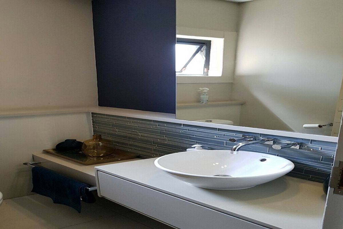 Modern office restroom featuring a sleek vessel sink, wall-mounted vanity, and contemporary tiled backsplash with a large integrated mirror.