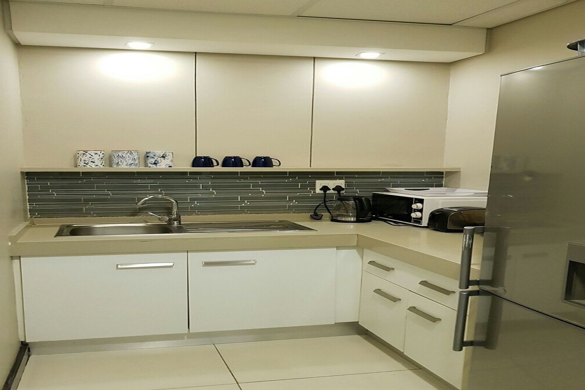 A compact office kitchenette featuring modern white cabinetry, a stone-look countertop, a stainless steel sink, and a tiled backsplash.