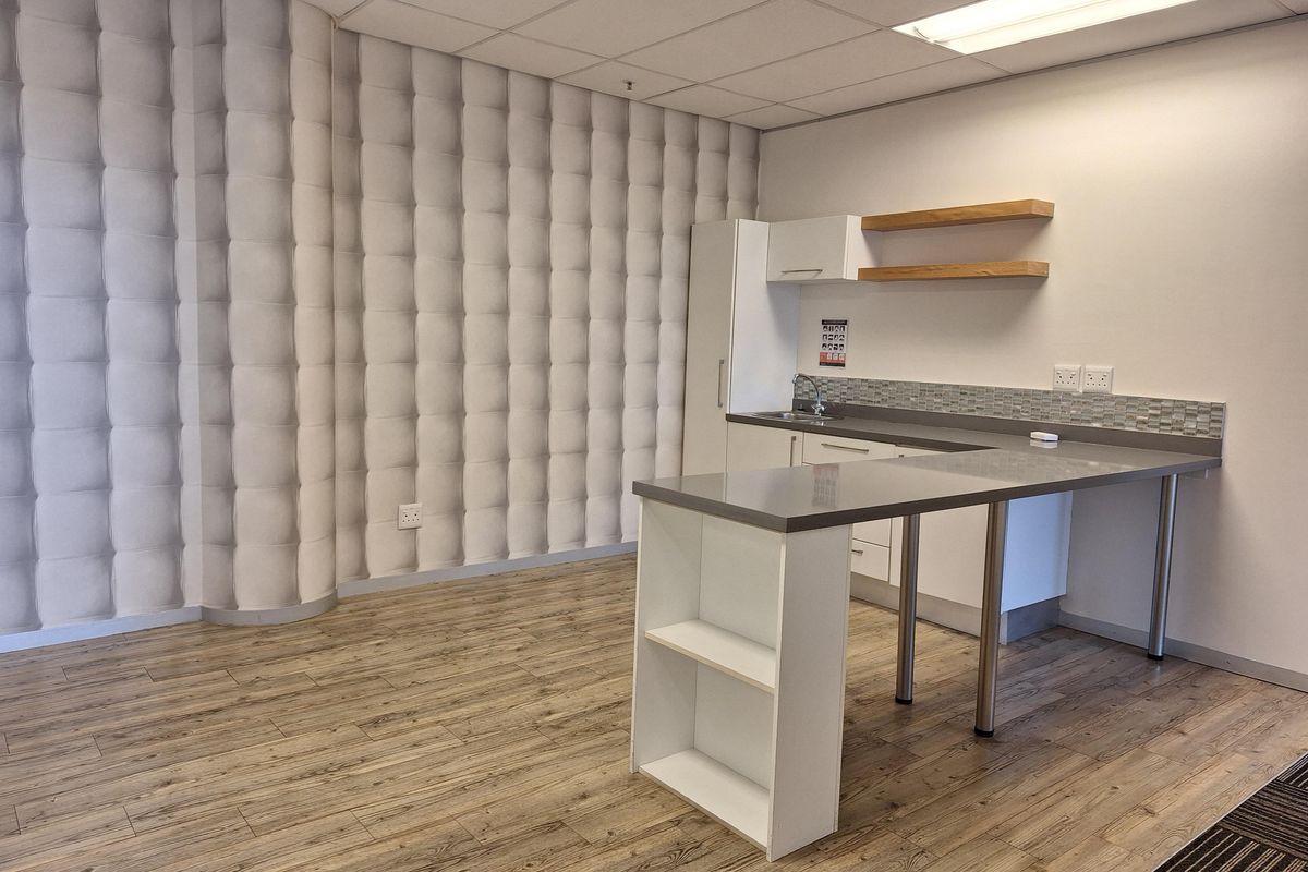 Modern office kitchenette featuring a stone countertop, integrated sink, floating wooden shelves, and wood-look flooring with a textured feature wall.