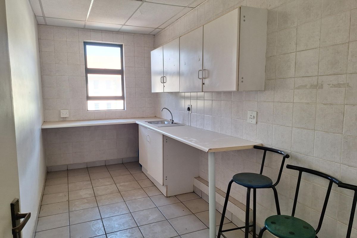 A functional office kitchenette featuring tiled walls, built-in cabinetry, a stainless steel sink, and a suspended ceiling.
