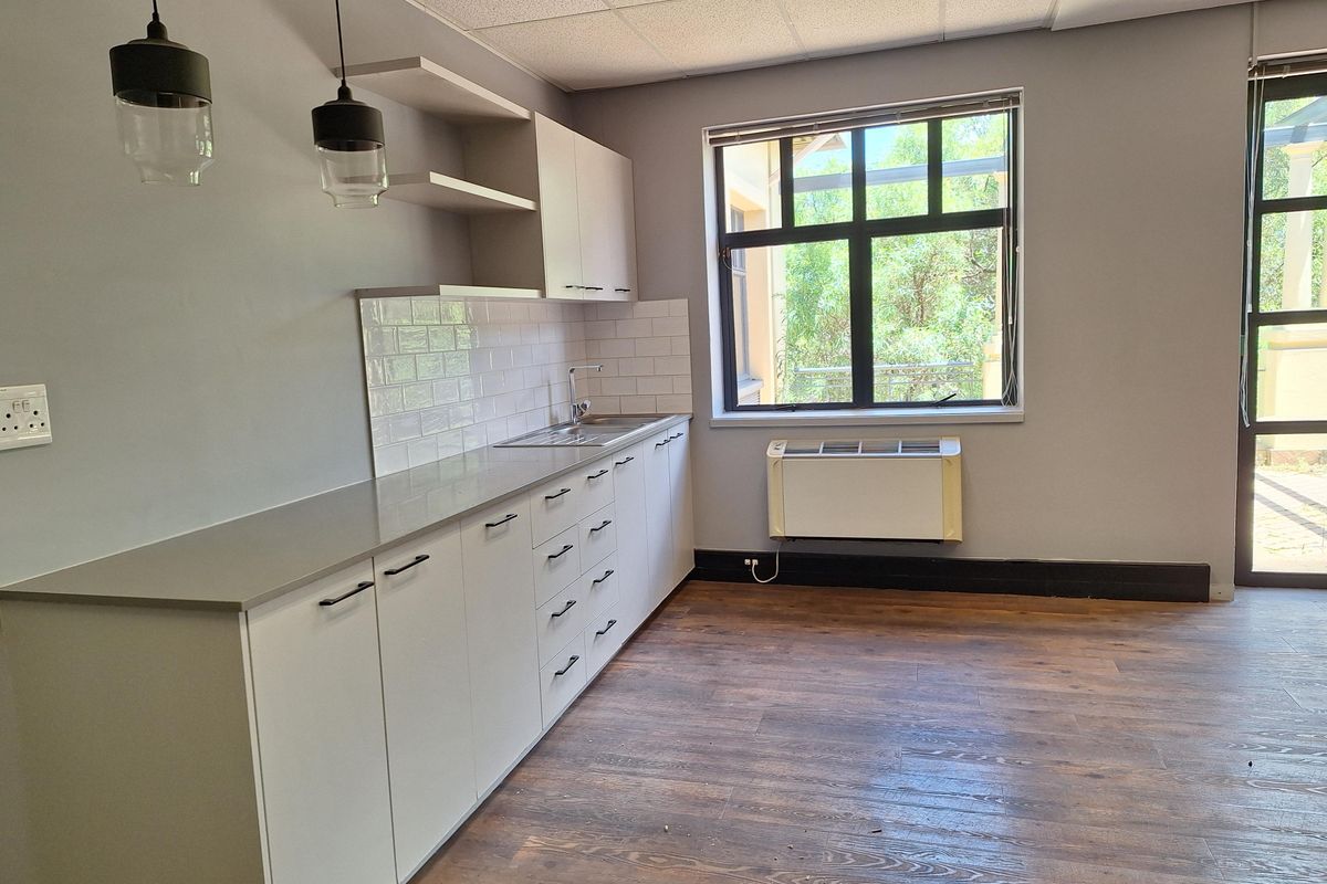 A modern office kitchenette featuring sleek white cabinetry, stone countertops, subway tile backsplash, and wood-look flooring with natural light.