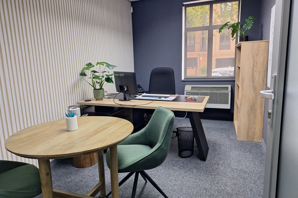 A professional office space featuring a window with natural light, carpeted flooring, and a wall-mounted HVAC unit.
