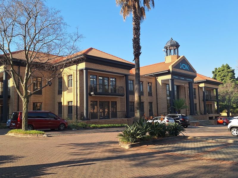 A professional office building featuring a brick facade, tiled roof, decorative cupola, and paved driveway entrance.