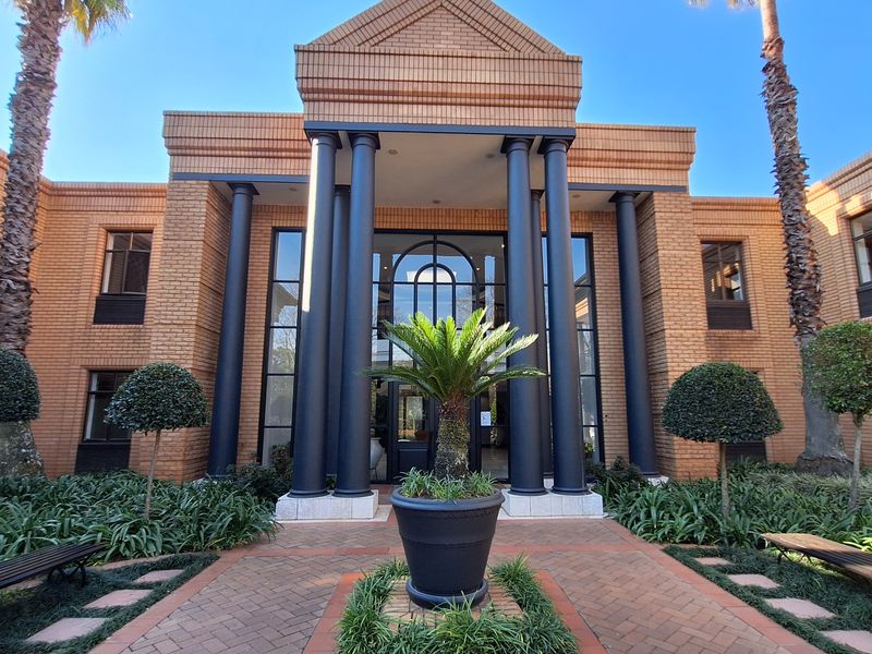 A professional front elevation of a brick office building featuring classical columns, a grand glass entrance, and a well-maintained paved courtyard.