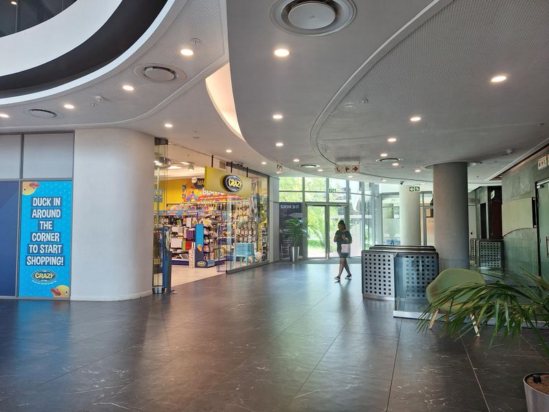 Modern office building lobby featuring polished tile flooring, recessed ceiling lighting, and glass storefront access to retail space.