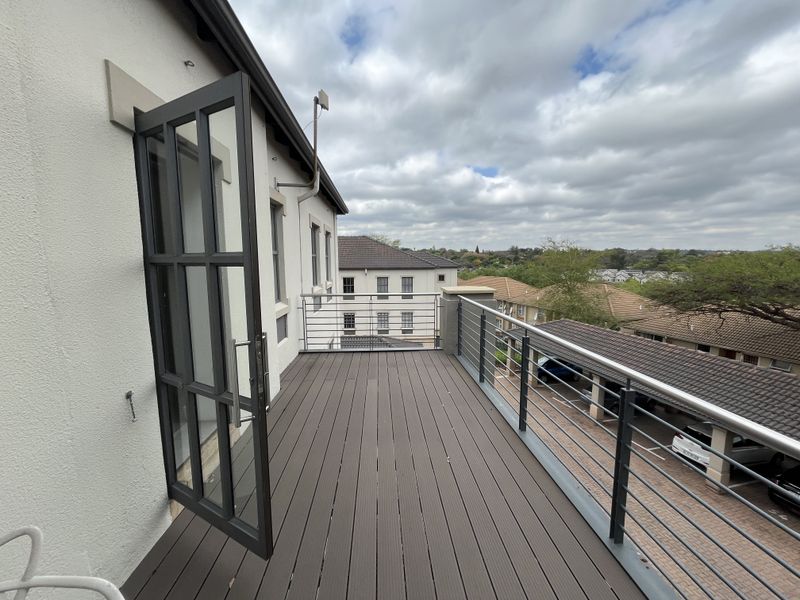 A spacious balcony featuring modern composite decking and secure metal railings, offering an elevated outdoor area accessible through a steel-framed glass door.