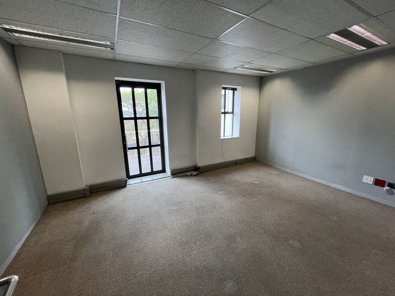 An empty office space featuring a suspended ceiling, recessed lighting, carpeted flooring, and a glass-paneled door leading to an outdoor area.