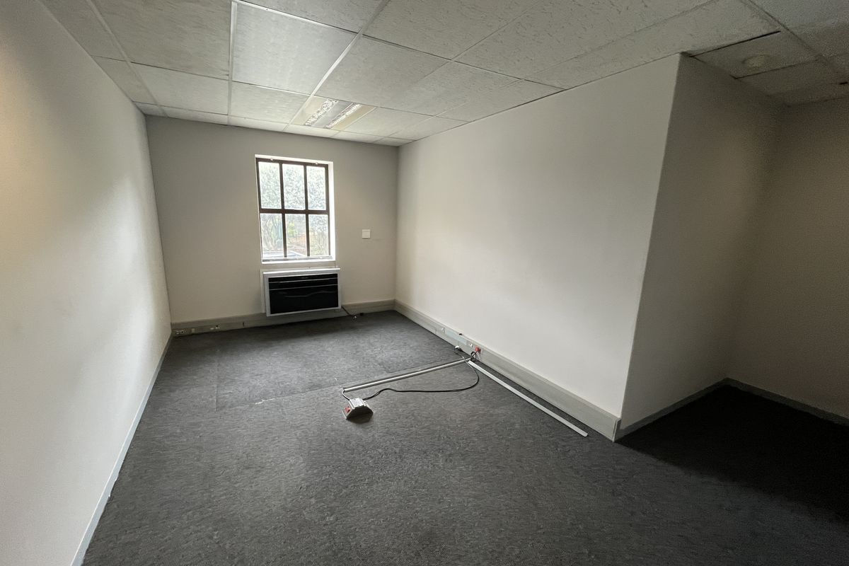 A vacant office space featuring a suspended ceiling, recessed lighting, carpeted flooring, and a wall-mounted air conditioning unit.