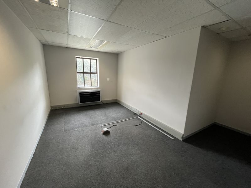 A vacant office space featuring a suspended ceiling, recessed lighting, carpeted flooring, and a wall-mounted air conditioning unit.