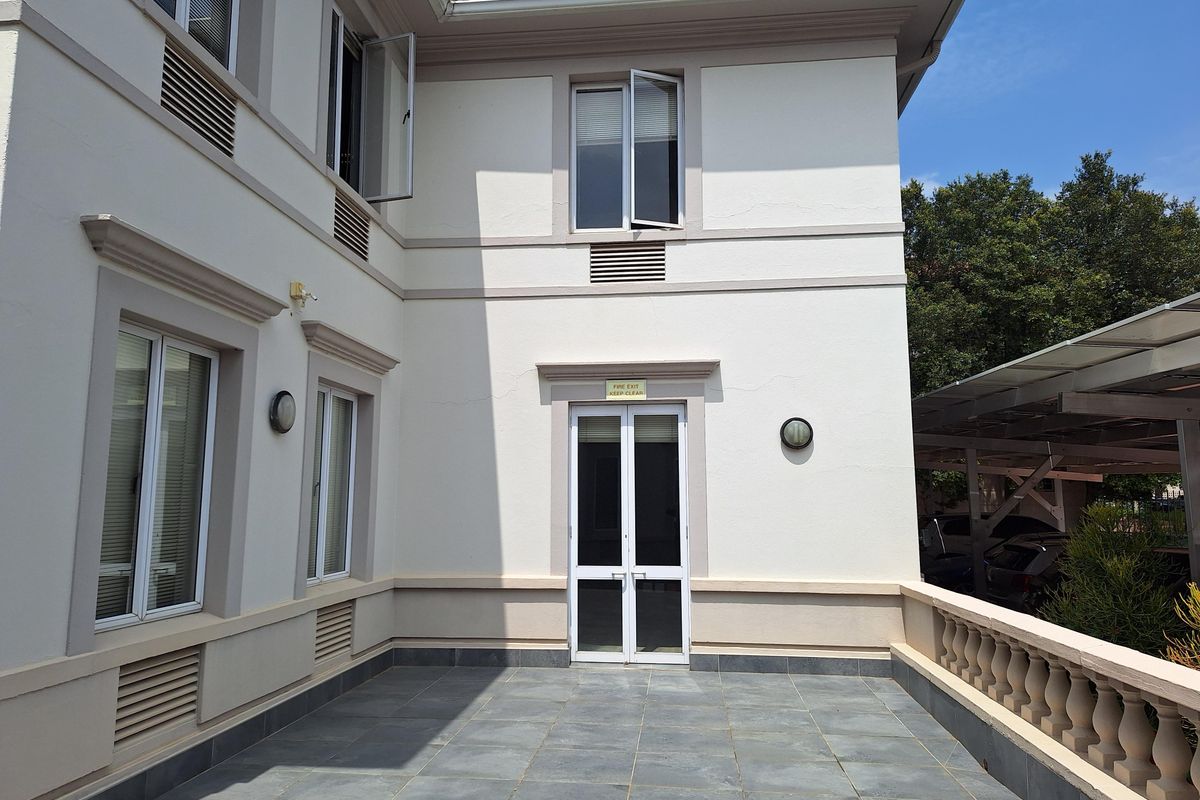 A well-maintained exterior rear patio area featuring tiled flooring, a fire exit door, and integrated wall-mounted lighting fixtures.