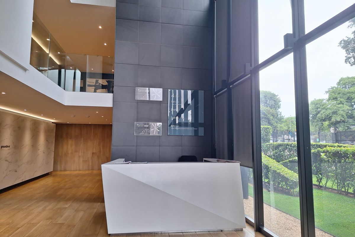 Modern office reception area featuring double-volume ceilings, floor-to-ceiling glass windows, tiled feature wall, and a contemporary white reception desk.