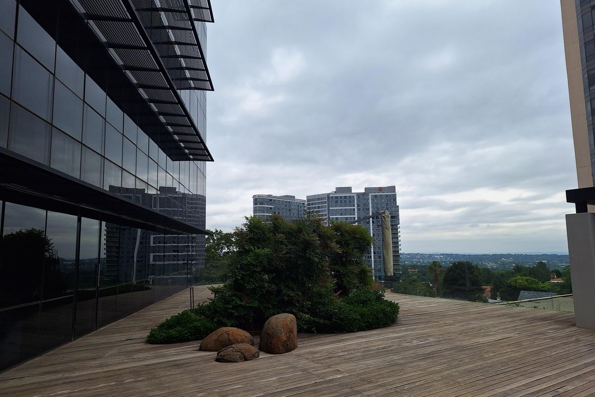 A modern outdoor terrace featuring timber decking, integrated landscaping with rocks, and expansive glass facade office building views.