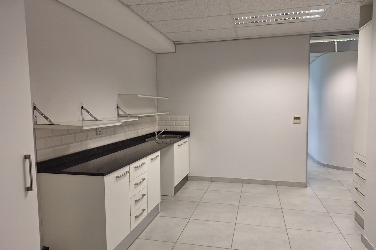 A clean, modern office kitchenette featuring white cabinetry, dark stone countertops, subway tile backsplash, and tiled flooring.