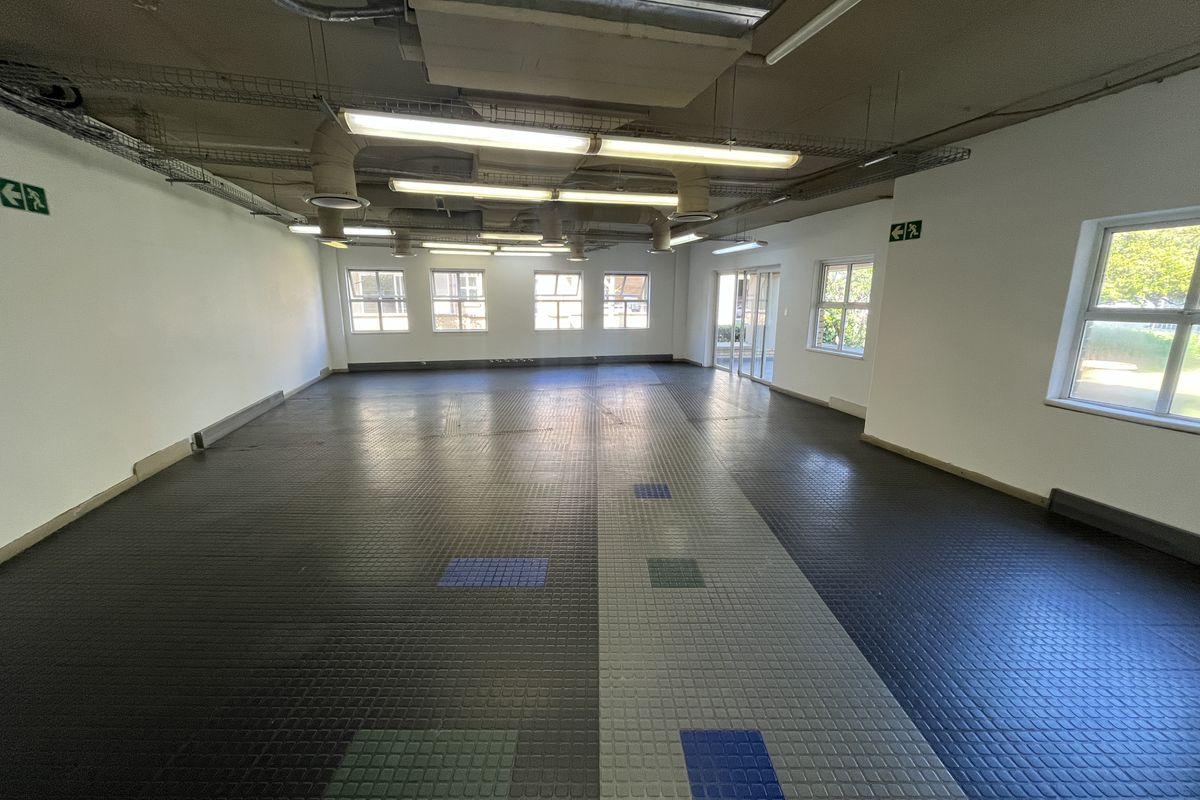 Spacious open-plan office area featuring exposed industrial ceiling ducting, durable rubber flooring, and ample natural light from multiple windows.