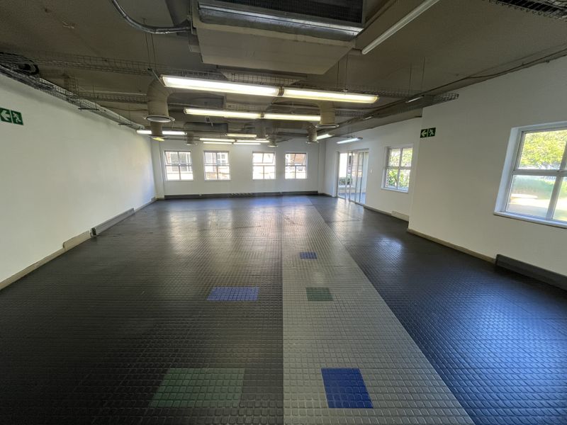 Spacious open-plan office area featuring exposed industrial ceiling ducting, durable rubber flooring, and ample natural light from multiple windows.