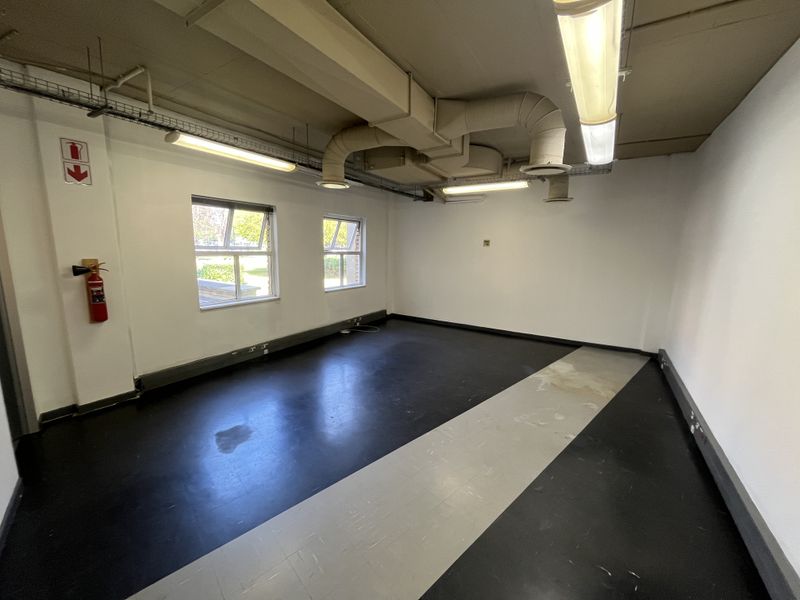 An empty office space featuring exposed HVAC ducting, fluorescent lighting, and durable vinyl flooring with integrated electrical trunking.