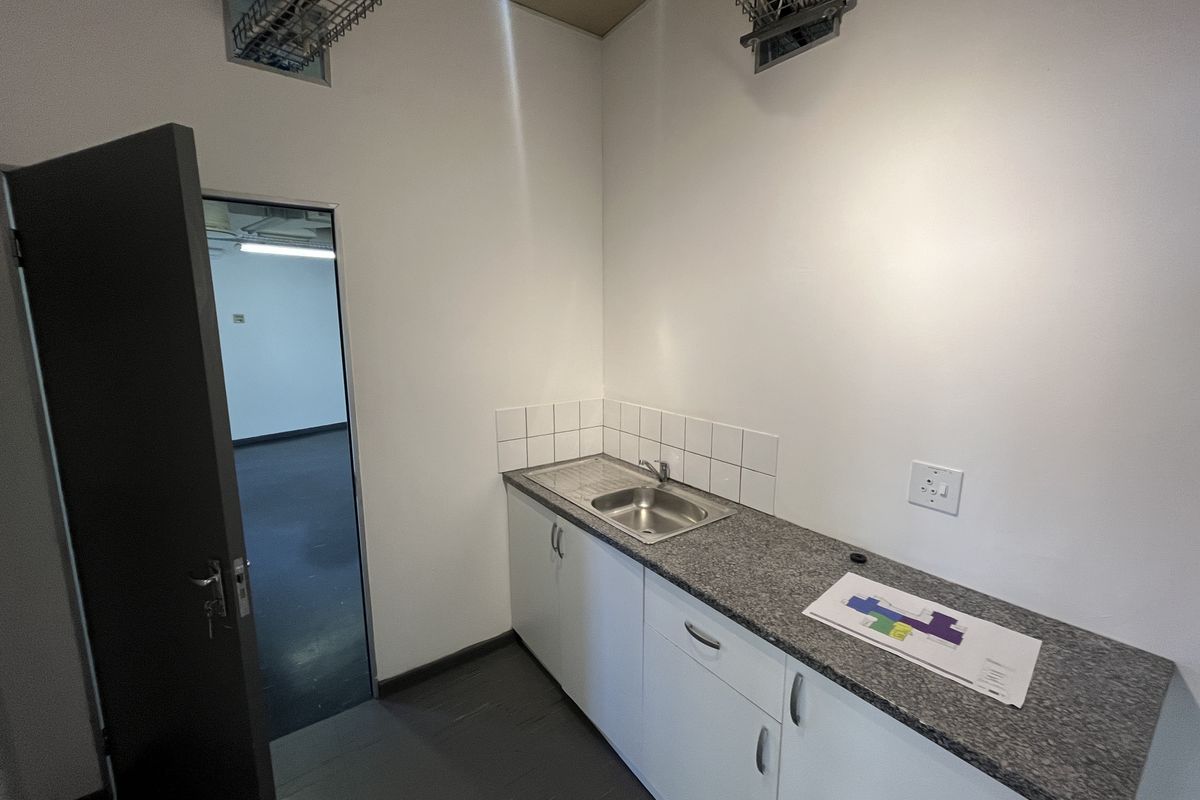 A compact office kitchenette featuring built-in cabinetry, a granite countertop, stainless steel sink, and tiled splashback, with exposed ceiling infrastructure.