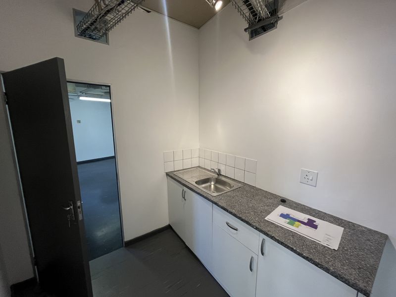 A compact office kitchenette featuring built-in cabinetry, a granite countertop, stainless steel sink, and tiled splashback, with exposed ceiling infrastructure.