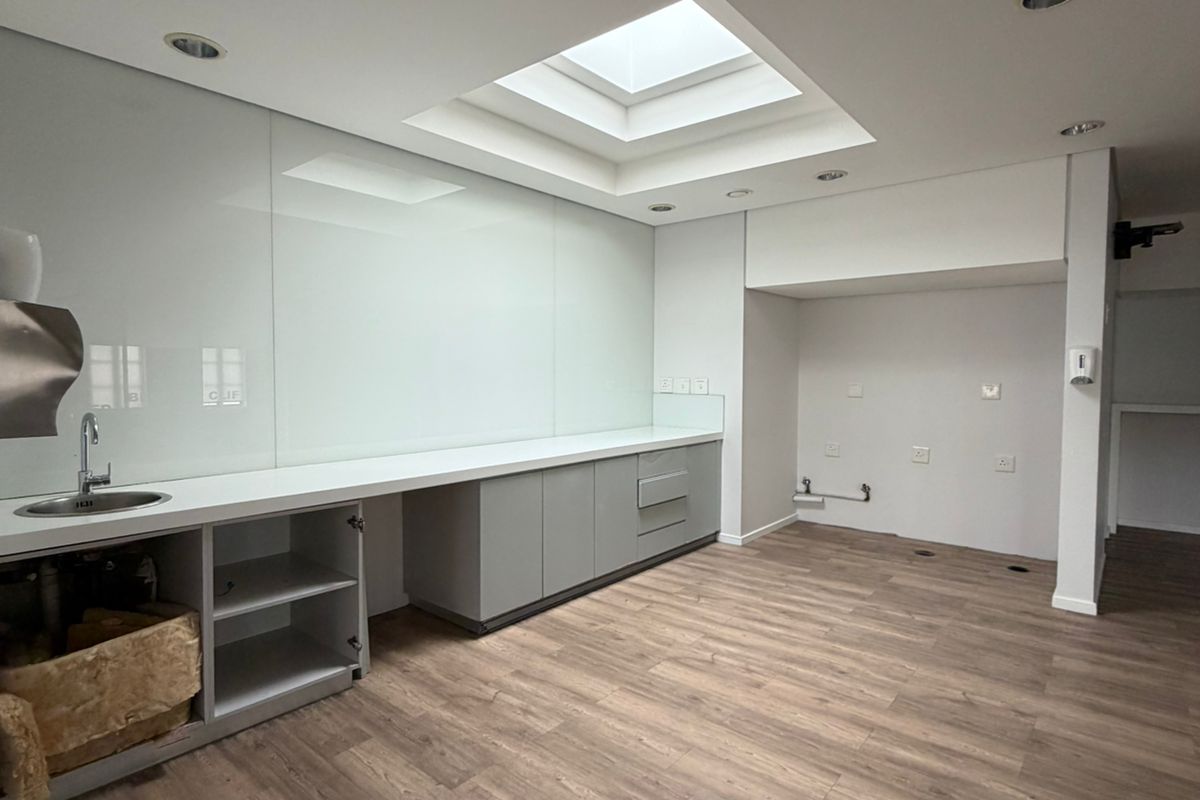 Modern office kitchenette featuring sleek grey cabinetry, a glass splashback, integrated sink, and a skylight providing ample natural light.