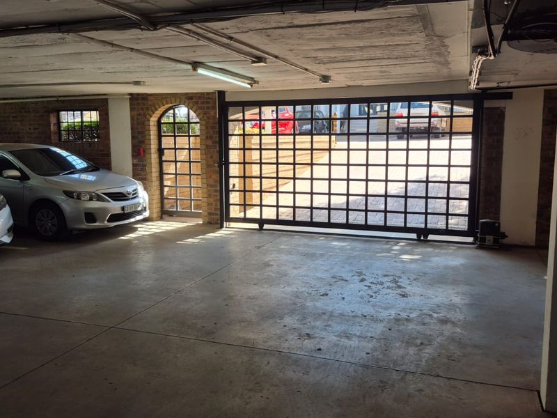 A functional covered parking garage featuring concrete flooring, exposed ceiling structure, and a secure metal gate entrance.