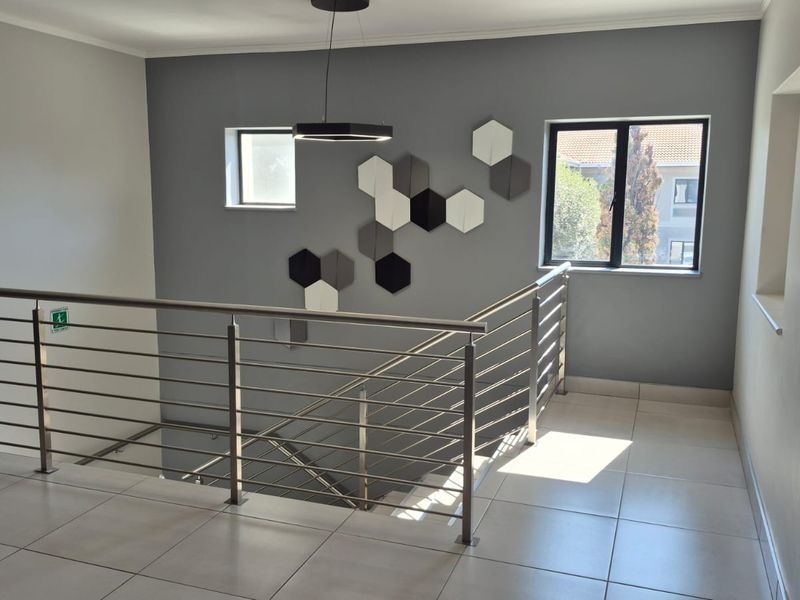 A bright, modern office hallway featuring tiled flooring, a stainless steel balustrade overlooking the staircase, and contemporary wall-mounted acoustic panels.