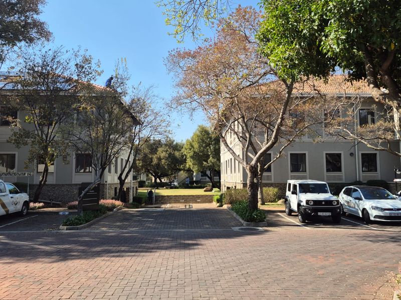 Front view of a professional office park complex featuring two multi-story buildings, paved parking area, and mature landscaped trees.