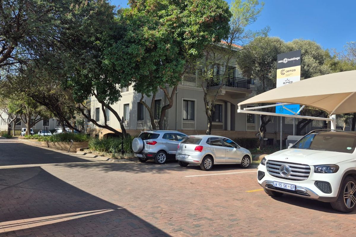 Exterior view of the office building featuring a paved parking area, shade cloth carports, and mature trees.