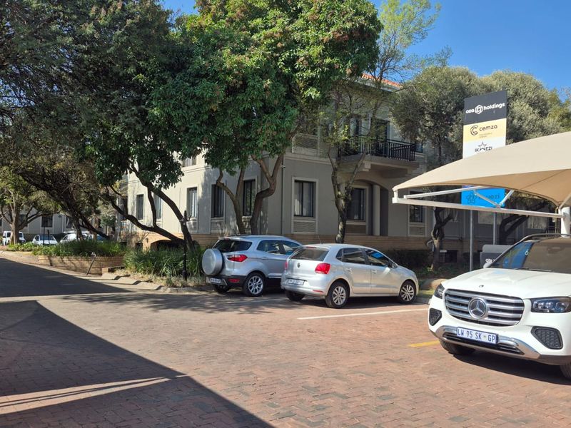 Exterior view of the office building featuring a paved parking area, shade cloth carports, and mature trees.
