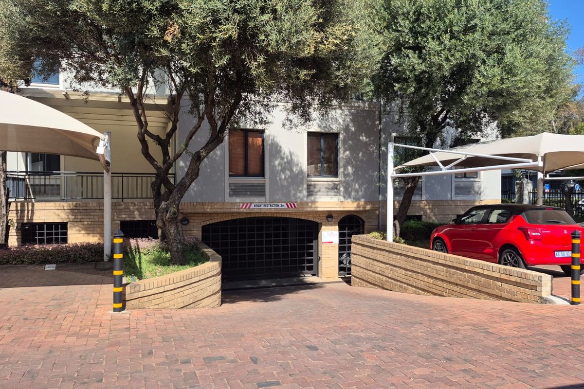 Front exterior view of the office building featuring a brick paved driveway, secure underground parking entrance, and shaded parking bays.