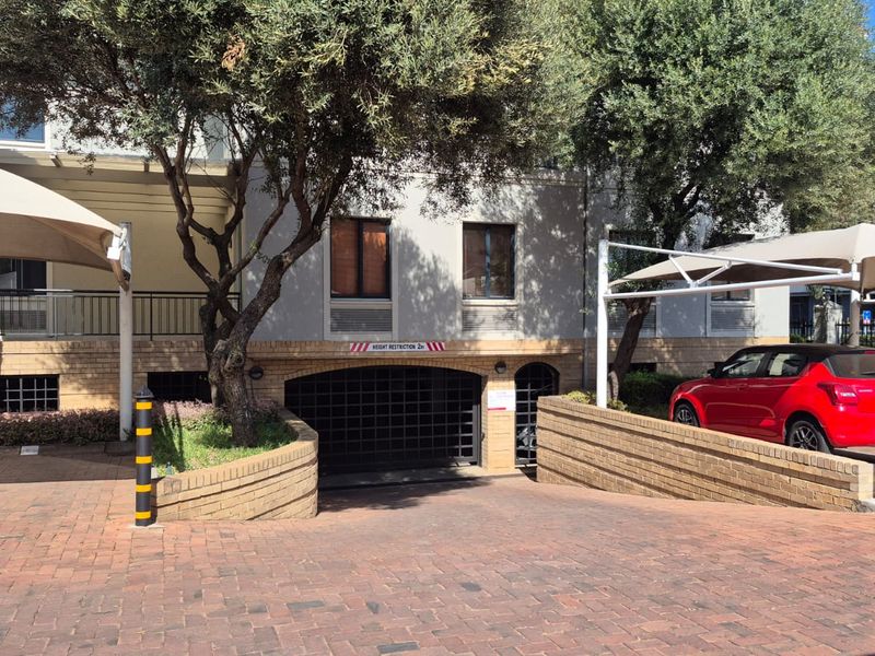 Front exterior view of the office building featuring a brick paved driveway, secure underground parking entrance, and shaded parking bays.