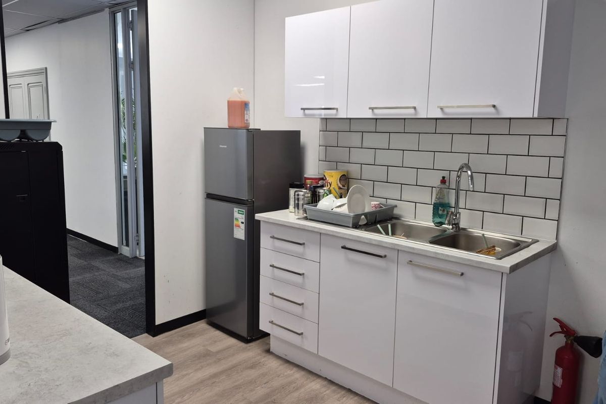 A compact office kitchenette featuring white cabinetry, a subway tile backsplash, and a stainless steel sink with a modern faucet.