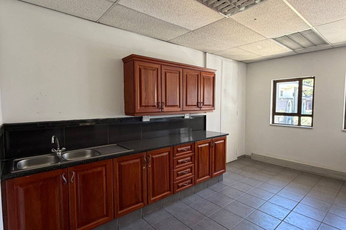 A functional office kitchenette featuring dark wood cabinetry, granite countertops, a stainless steel sink, and a suspended acoustic tile ceiling.