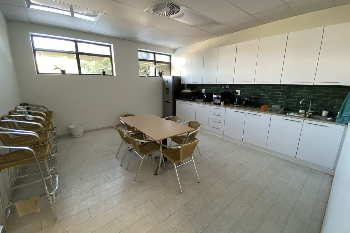 A functional office kitchenette featuring white cabinetry, a dark green tiled backsplash, stainless steel sink, and a suspended ceiling with integrated lighting.