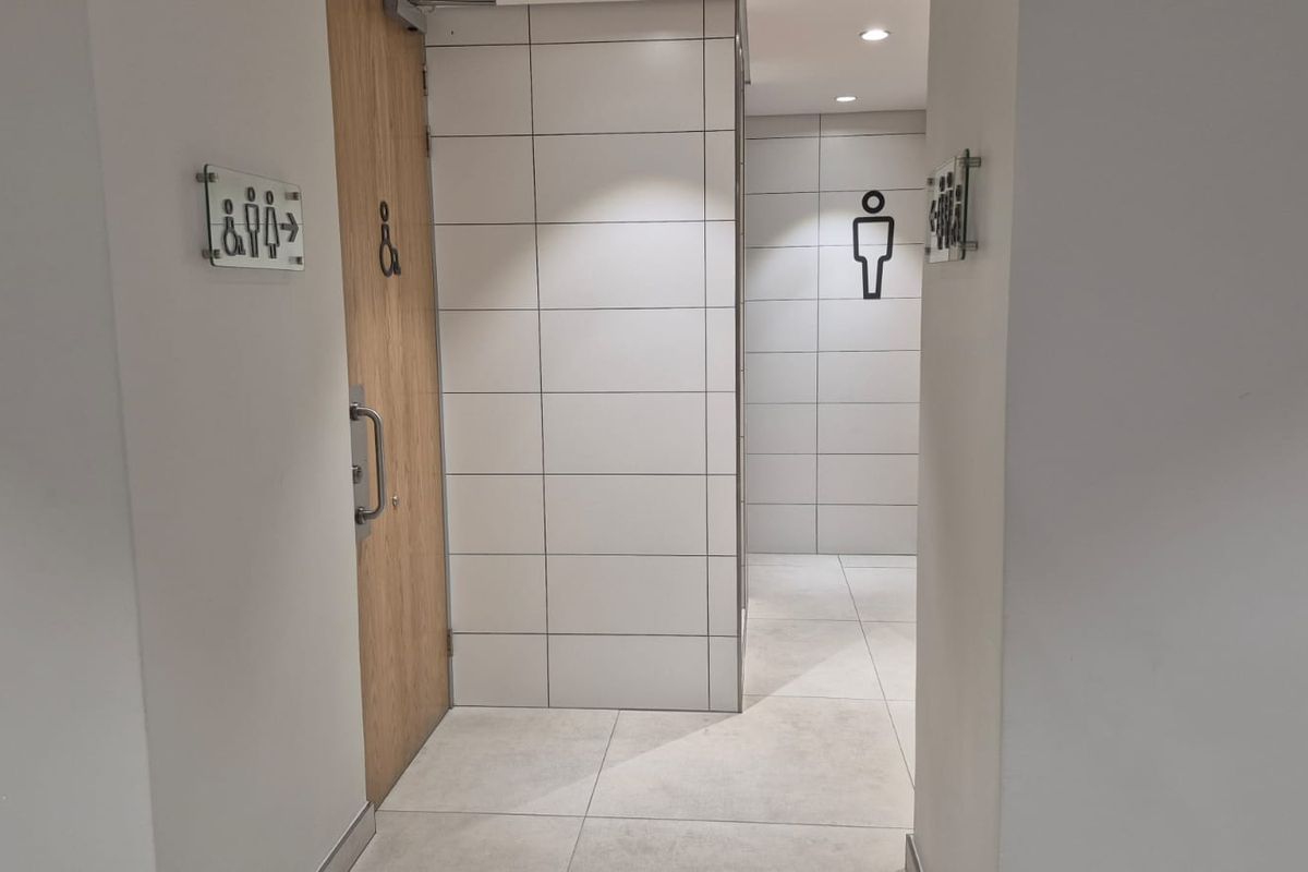 A clean and modern office restroom entrance featuring tiled walls, flooring, and clear signage for accessibility and gender-specific facilities.