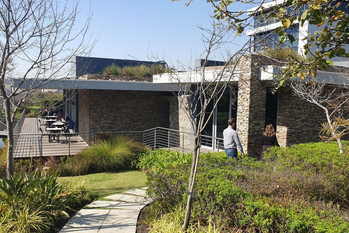 Modern office building exterior featuring stone cladding, a raised wooden deck patio area, and landscaped garden surroundings with a paved walkway.