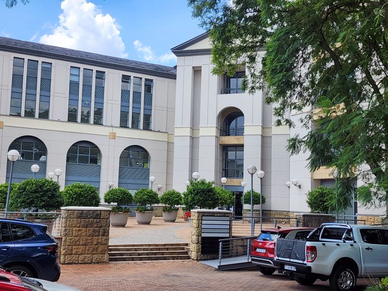 A well-maintained multi-story office building facade featuring stone cladding, arched windows, and a paved courtyard entrance area.