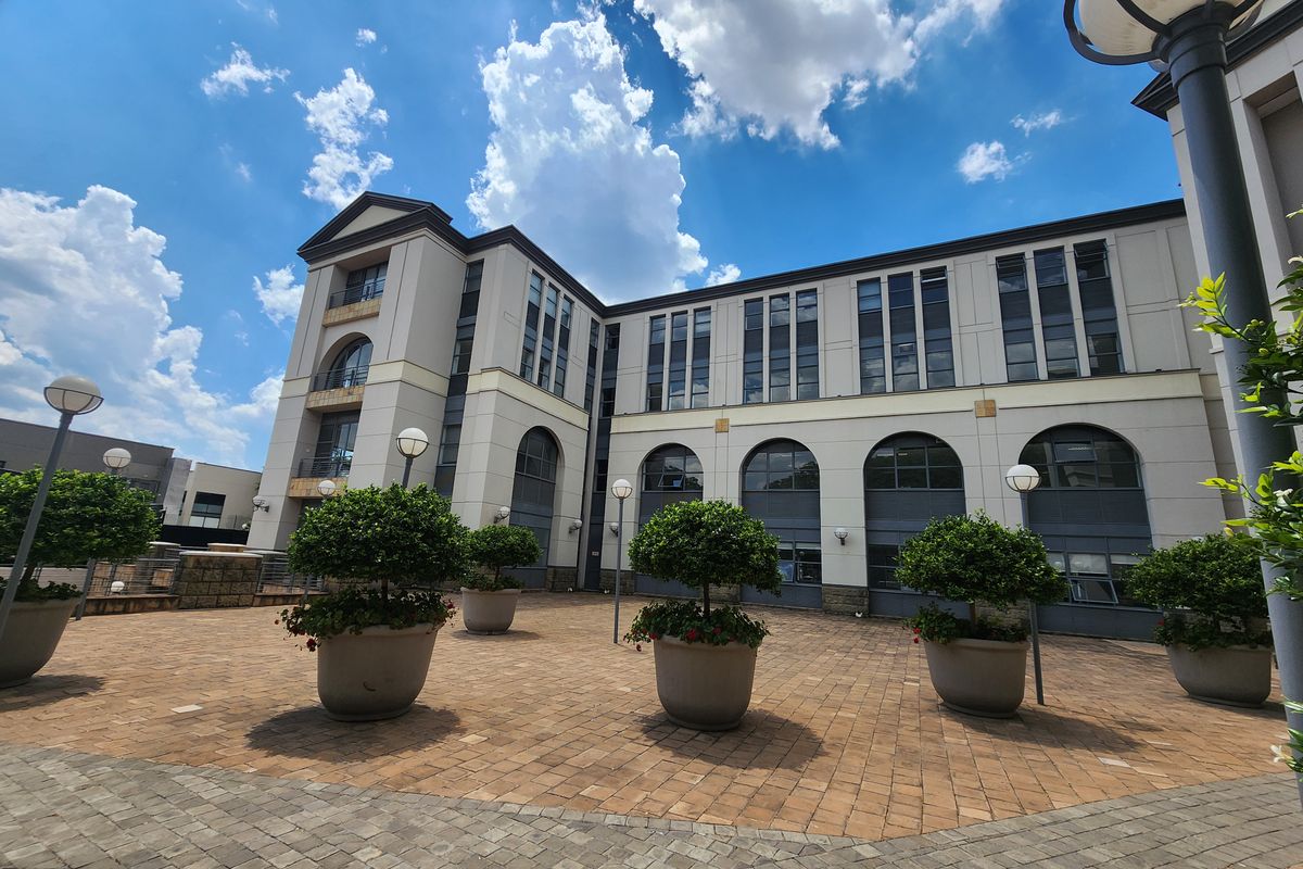 A well-maintained multi-story office building exterior featuring a paved courtyard, arched architectural detailing, and integrated exterior lighting.