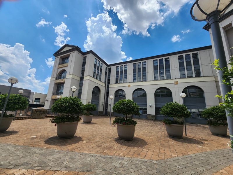 A well-maintained multi-story office building exterior featuring a paved courtyard, arched architectural detailing, and integrated exterior lighting.